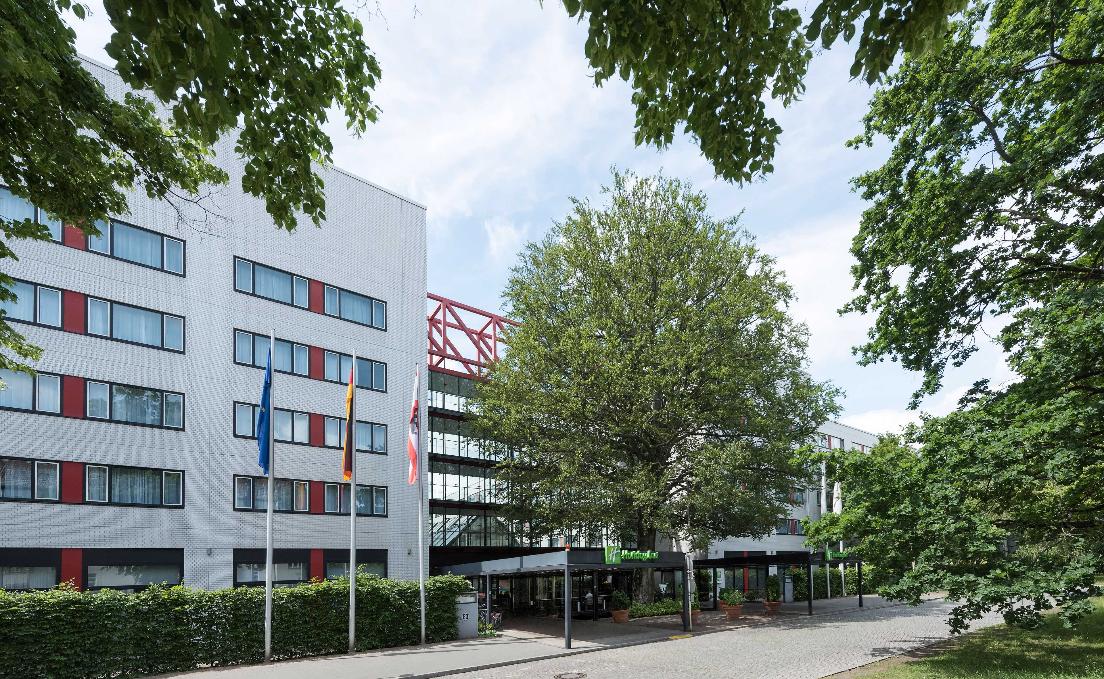 A modern hotel exterior with flags and lush trees under a clear sky creates a welcoming atmosphere.