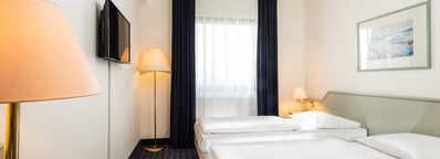 Ein helles Zweibettzimmer mit zwei Einzelbetten, einem Fernseher und gemütlicher Beleuchtung lädt zum Entspannen ein.