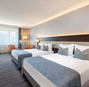 Ein modernes Hotelzimmer mit zwei Doppelbetten, einem Schreibtisch und einem großen Fenster sorgt für eine entspannte Atmosphäre.