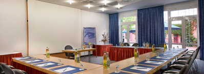 Ein heller Konferenzraum mit U-förmig angeordneten Tischen, Notizblöcken und Getränken, ideal für Meetings.