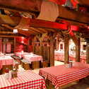A cozy alpine cabin interior features wooden tables covered with red checkered tablecloths, creating a warm and inviting atmosphere.