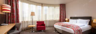 Ein komfortables Hotelzimmer mit großem Bett, rotem Sessel und schicker Dekoration lädt zum Entspannen ein.