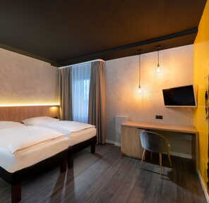 Ein modernes Familienzimmer mit Doppelbett, stilvoller Wandkunst und einem Schreibtisch unter warmen Hängelampen.