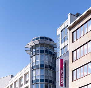 Modern hotel exterior with a cylindrical glass tower and Mercure signage against a clear blue sky. | © Abaca PressGuido Erbring
