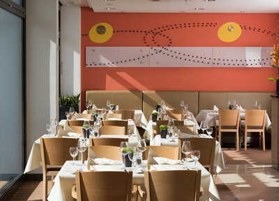 Ein stilvolles Restaurant mit gedeckten Tischen und moderner Wandkunst lädt zum entspannten Essen ein.