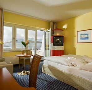 Ein gemütliches Standardzimmer mit gelben Wänden, einem Doppelbett, Schreibtisch und einem kleinen Tisch am Fenster.