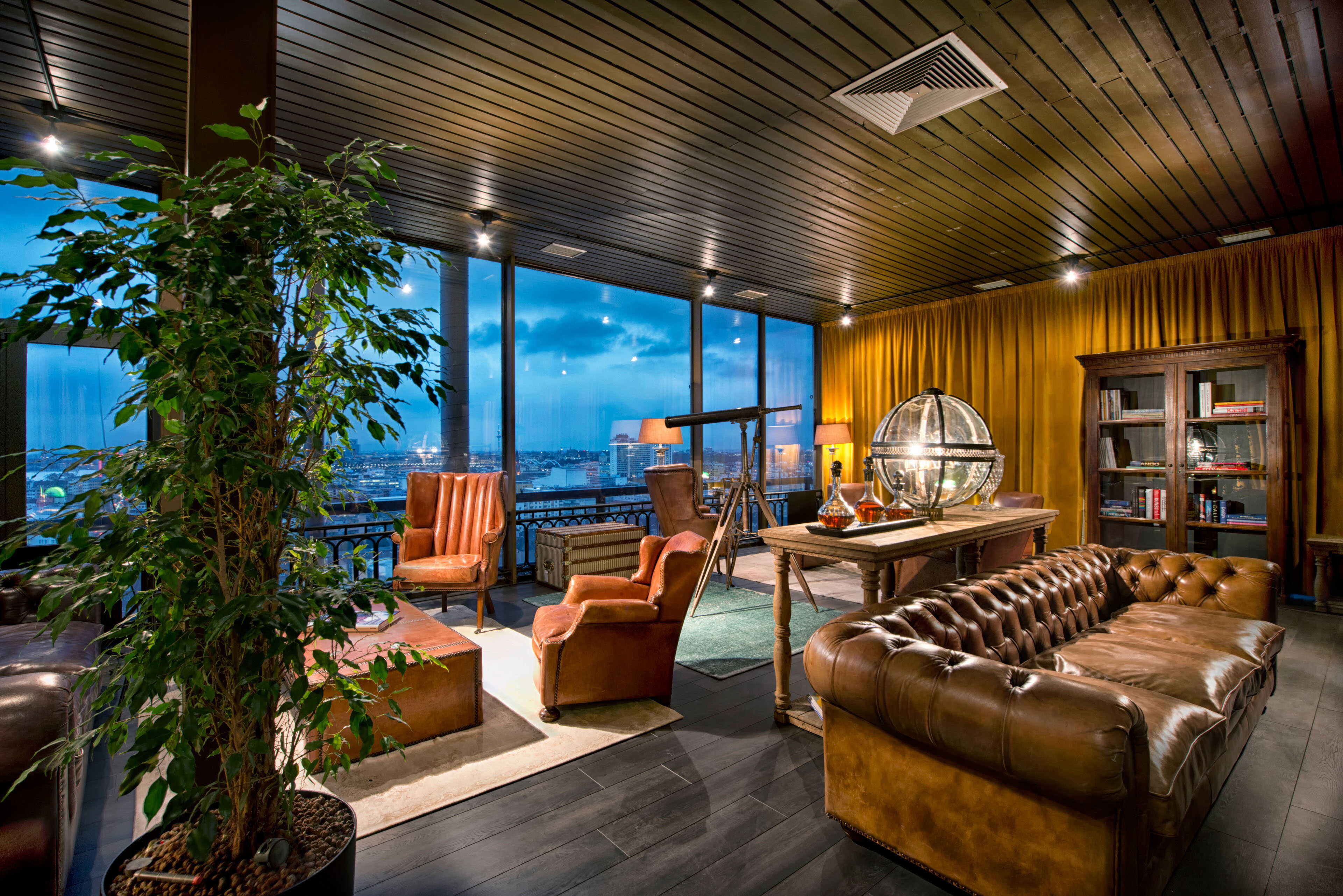 A luxurious lounge features leather seating, a telescope, and a city view through large windows, creating an elegant ambiance.