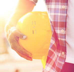 Eine Person hält einen gelben Bauhelm in der Hand, während die Sonne im Hintergrund scheint.