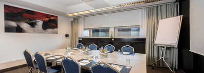 Ein moderner Meetingraum mit einem Tisch, umgeben von blauen Stühlen, ist für eine Besprechung vorbereitet.