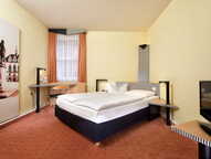 Ein gemütliches Doppelzimmer mit einem großen Bett, einem Schreibtisch und einem Kunstwerk an der Wand.