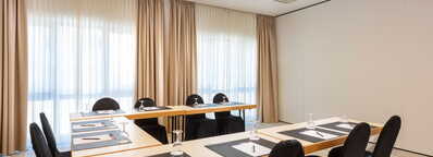 Ein heller Meetingraum mit U-förmiger Tischanordnung und gedeckten Stühlen, bereit für eine Konferenz in Kampenwand.