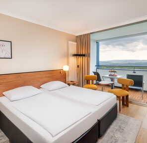 Ein modernes Hotelzimmer mit Doppelbett und Balkon bietet eine atemberaubende Aussicht auf die Landschaft.