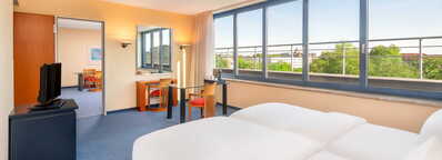 Ein modernes Hotelzimmer mit großen Fenstern bietet einen Blick auf die grüne Umgebung und verfügt über einen Esstisch.