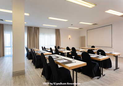 Ein heller Seminarraum mit Tischen und Stühlen ist für eine Konferenz vorbereitet.