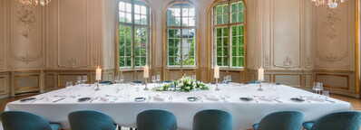 Ein eleganter Speisesaal mit einem festlich gedeckten Tisch, umgeben von blauen Stühlen und großen Fenstern.