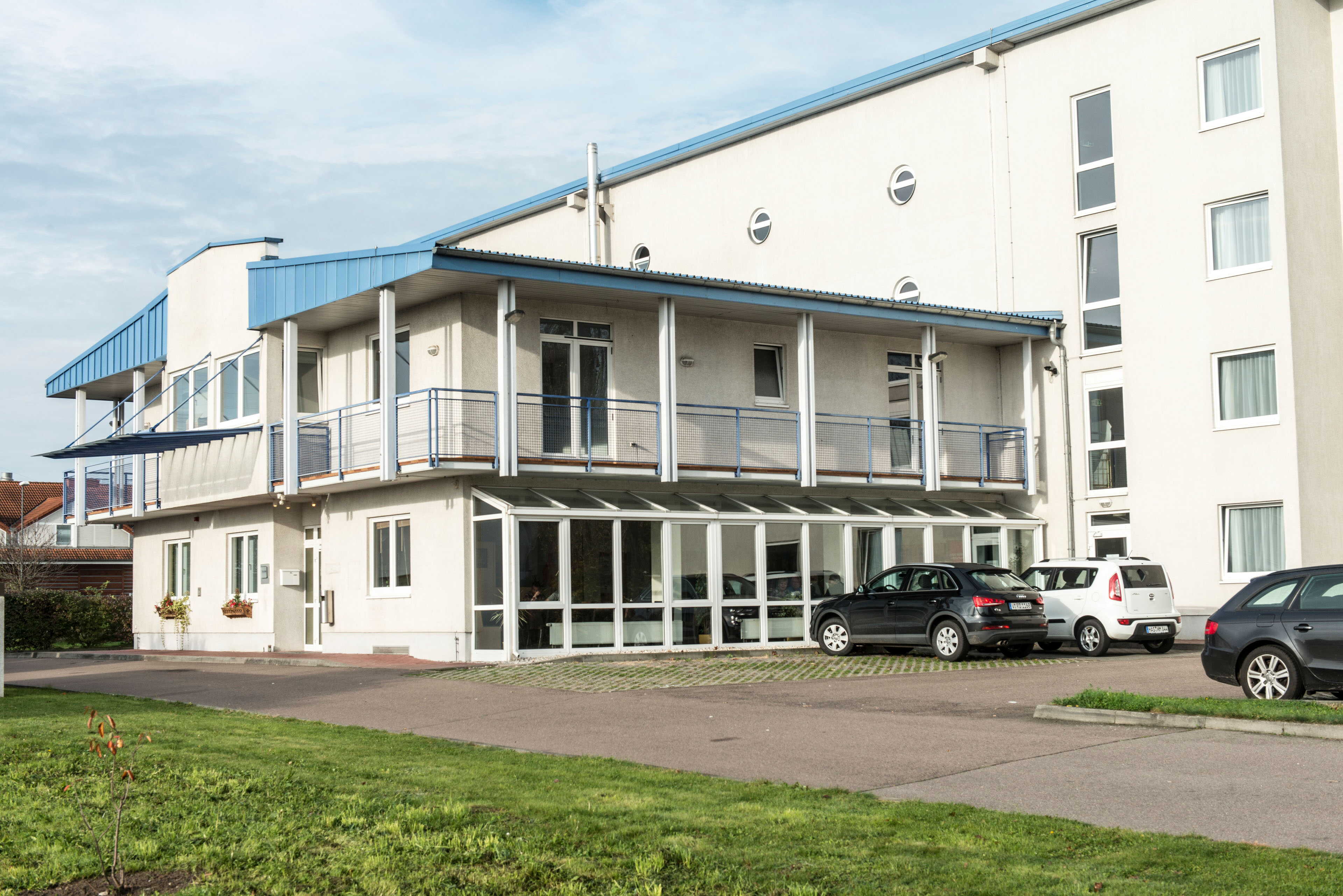 A modern building with a blue roof features parked cars outside and a well-maintained grassy area in the foreground.