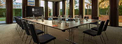 Ein moderner Konferenzraum im Wasserturm Deluxe mit Tischen, Stühlen und Wasserflaschen, umgeben von großen Fenstern.