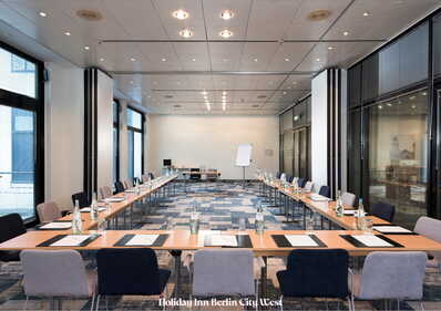 Ein moderner Konferenzraum mit U-förmiger Tischanordnung und Schreibmaterialien ist für ein Meeting vorbereitet.