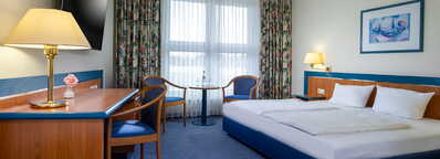 Ein gemütliches Hotelzimmer mit Doppelbett, Schreibtisch und Fernseher lädt zum Entspannen ein.