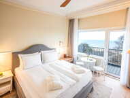 A deluxe hotel room features a cozy bed and a balcony with a stunning ocean view.
