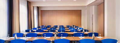 Ein Konferenzraum mit blauen Stühlen und Tischen ist für ein Meeting vorbereitet, mit Wasserflaschen und Gläsern.