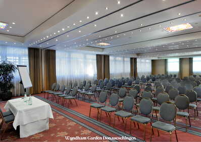 Ein leerer Konferenzraum im Wyndham Garden Donaueschingen mit Stuhlreihen und einem vorbereiteten Tisch vorne.
