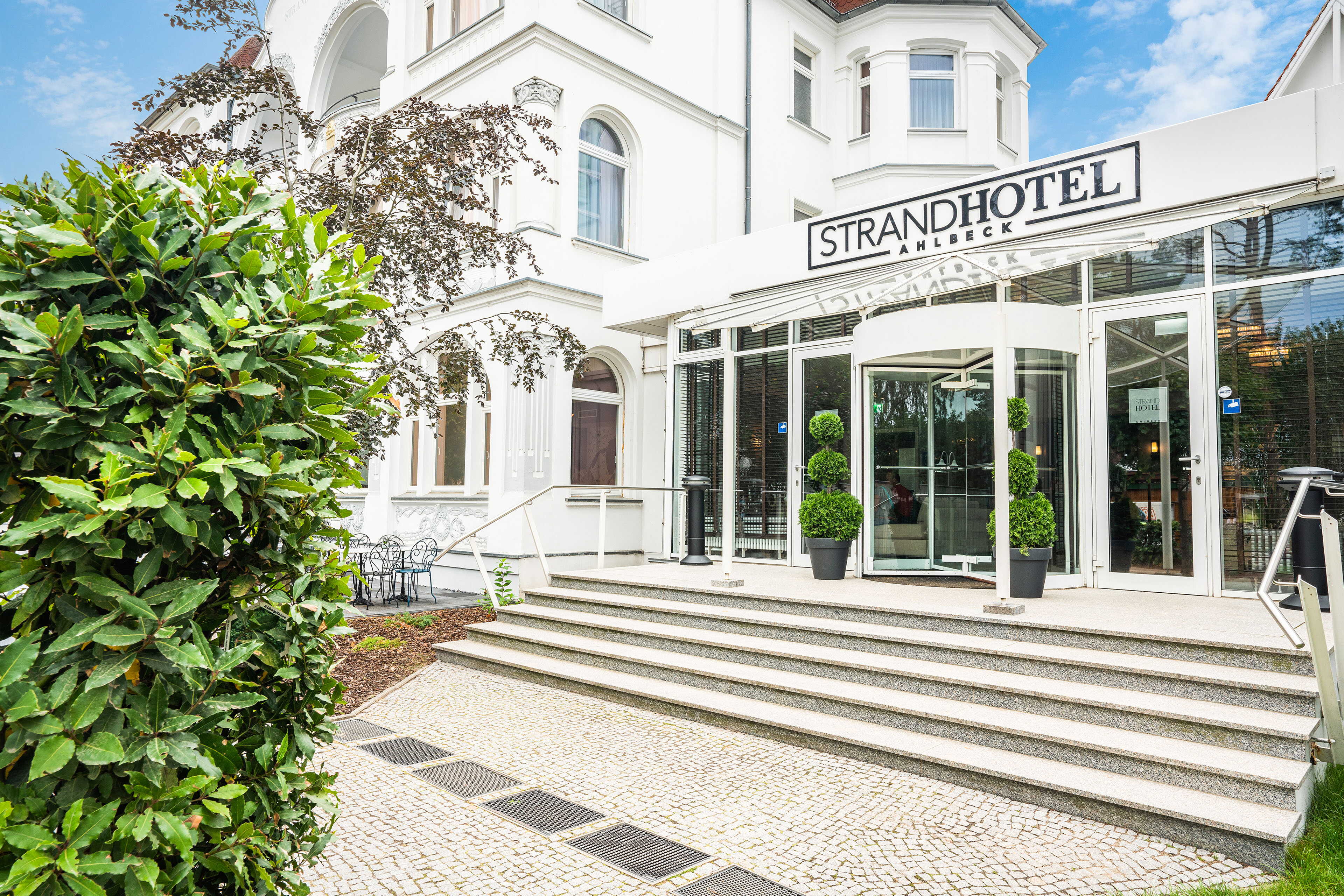 The exterior of Strandhotel Ahlbeck features elegant architecture with lush greenery and a welcoming entrance.