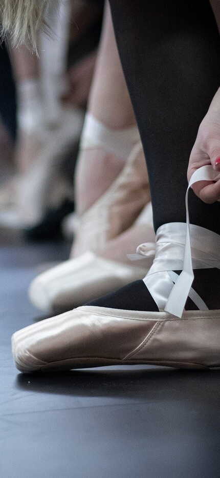 Tänzerinnen binden ihre Ballettschuhe, während sie sich auf eine Probe vorbereiten.