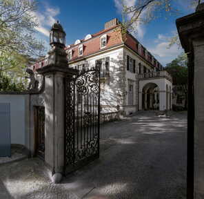 Ein elegantes Eingangstor führt zu einem stilvollen Hotelgebäude mit rotem Dach und klassischer Architektur.