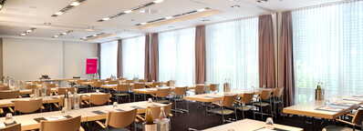 Ein heller Konferenzraum mit vielen Tischen und Stühlen ist für ein Meeting vorbereitet.