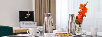 Auf einem Konferenztisch im Georgengarten stehen Kaffeekannen, Tassen, Kekse und eine Vase mit orangefarbenen Blumen.