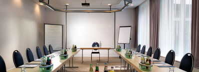 Ein heller, moderner Meetingraum in Hessen mit U-förmiger Tischanordnung, Getränken und Schreibmaterialien.