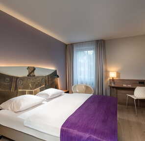 Ein modernes Doppelzimmer mit lila Akzenten und stilvollem Schreibtisch bietet eine einladende Atmosphäre.