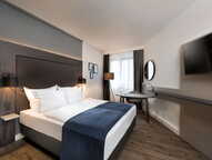 A modern business room features a queen-size bed, sleek furniture, and a wall-mounted TV for a comfortable stay.