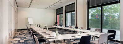 Ein moderner Besprechungsraum mit U-förmiger Tischanordnung, Stühlen und Flipchart, bereit für ein Meeting.