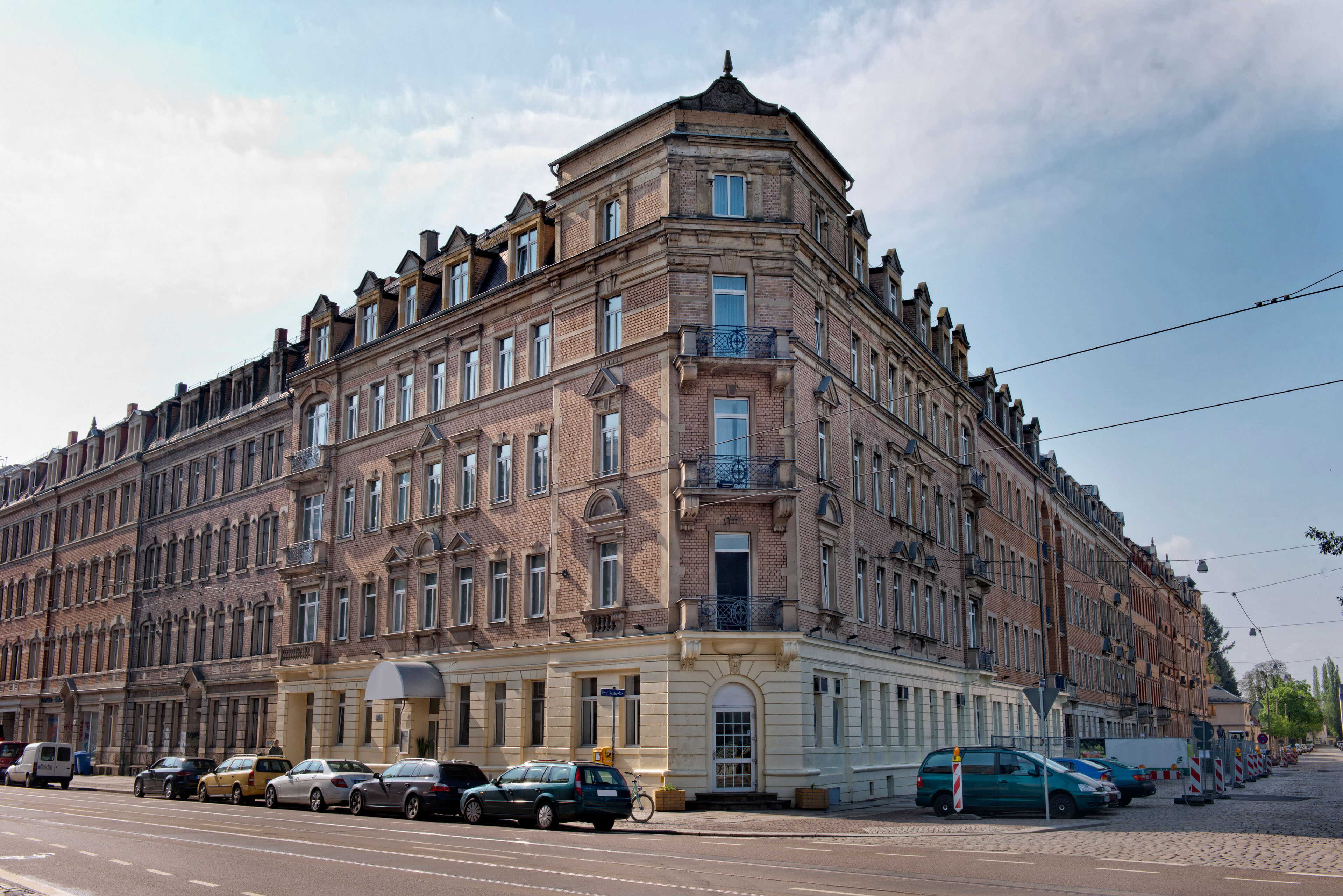 Historic brick building on a city corner with parked cars lining the street under a clear sky.