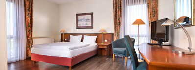 Ein gemütliches Doppelzimmer mit Holzboden, einem großen Bett, Schreibtisch und Fernseher, ideal für einen erholsamen Aufenthalt.