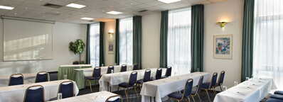 Ein heller Meetingraum mit Tischen, Stühlen und einem Projektor ist für eine Präsentation vorbereitet.