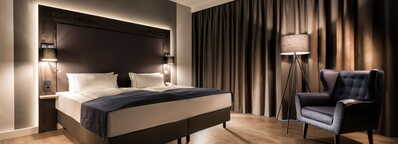 Ein stilvolles Hotelzimmer mit einem großen Doppelbett, weichen Kissen und einem bequemen Sessel lädt zum Entspannen ein.