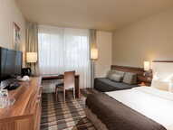 Ein modern eingerichtetes Standardzimmer mit Doppelbett, Schreibtisch, Flachbildfernseher und gemütlicher Beleuchtung.