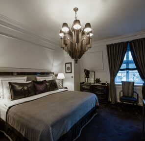 Eine elegante Premium Junior Suite mit luxuriösem Bett, stilvoller Beleuchtung und einem Fenster mit schweren Vorhängen.