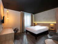 A modern standard room features a cozy bed, a sleek desk, and warm lighting, creating a welcoming atmosphere.