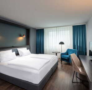 Ein modernes Doppelzimmer mit gemütlichem Bett, blauen Vorhängen und stilvollen Lampen lädt zum Entspannen ein.