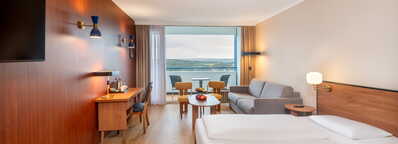 Ein modernes Hotelzimmer mit Doppelbett, Schreibtisch und Balkon mit Blick auf die Landschaft.