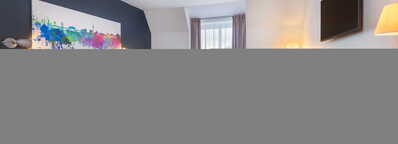 Modernes Hotelzimmer mit Doppelbett, farbenfrohem Kunstwerk an der Wand, gemütlicher Sitzecke und großem Fenster.