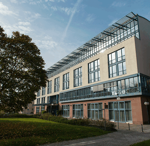 A modern building with large windows stands adjacent to a lush green park under a clear blue sky.