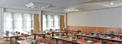 Ein heller Konferenzraum ist für ein geschäftliches Meeting vorbereitet, mit Tischen, Stühlen und Getränken.