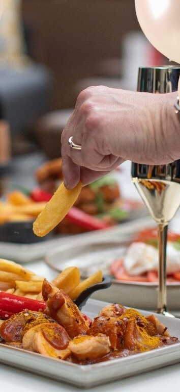 Eine Hand greift nach Pommes auf einem Tisch mit Partyballons und Sektgläsern.