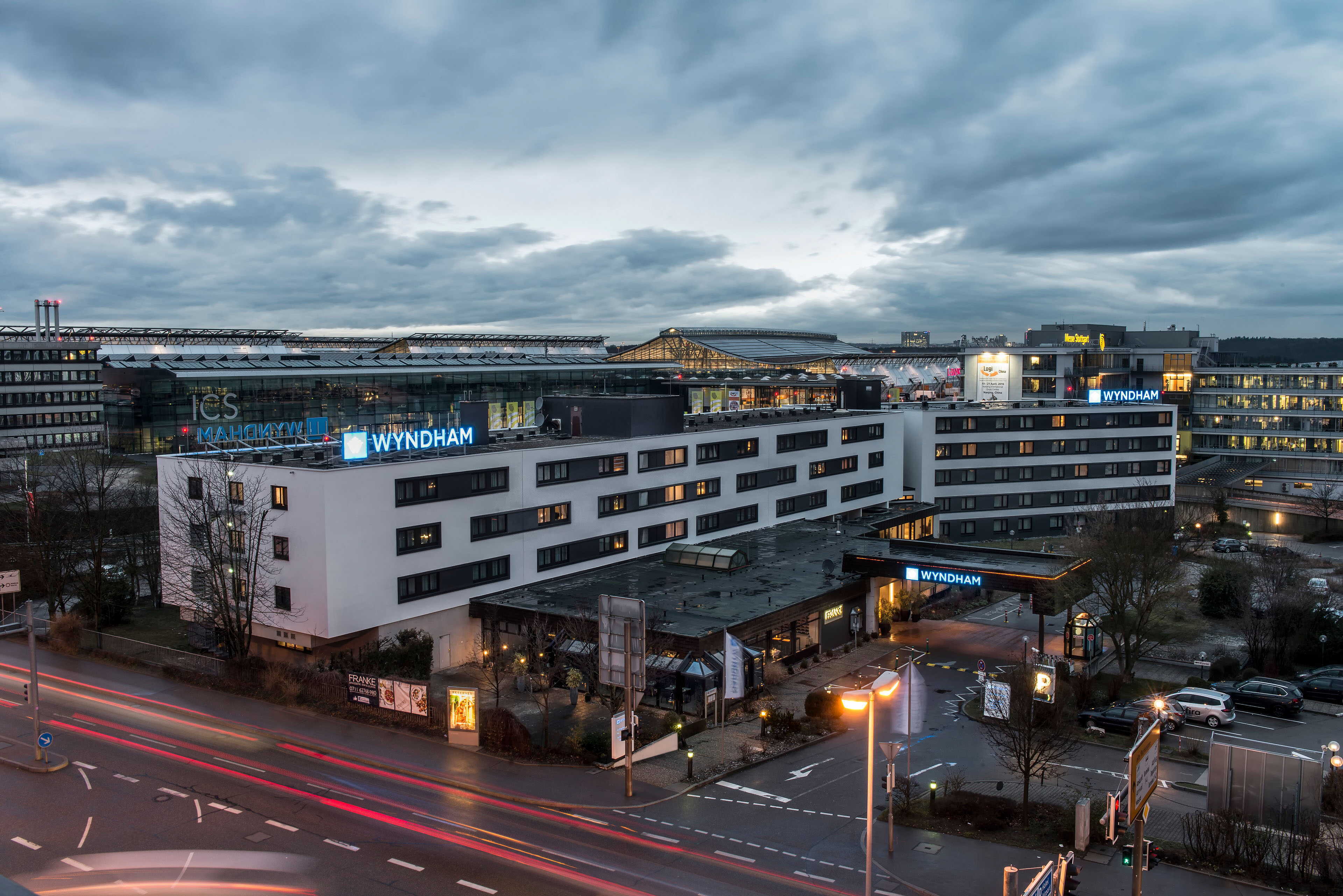 A bustling evening scene shows the exterior of the Wyndham Hotel near ICS, with traffic lights illuminating the street.