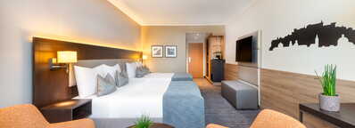 Ein modernes Hotelzimmer mit zwei Betten, gemütlichen Sesseln und einer stilvollen Wanddekoration lädt zum Entspannen ein.